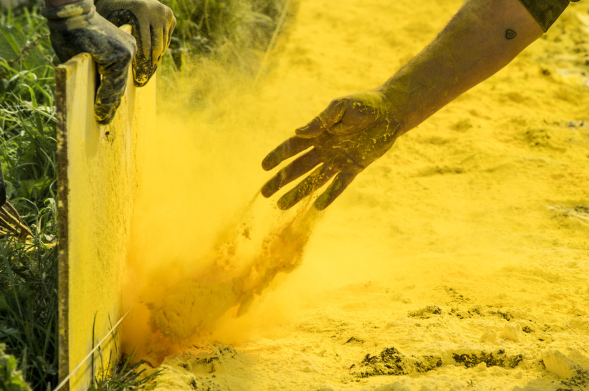 A hand throws yellow dust against a board in an attempt to draw a line on some grass.